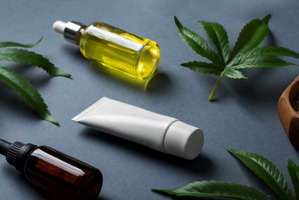 Gemini said A dark tabletop display featuring glass droppers and a cosmetic tube among hemp leaves, representing various products for a WooCommerce CBD shop.