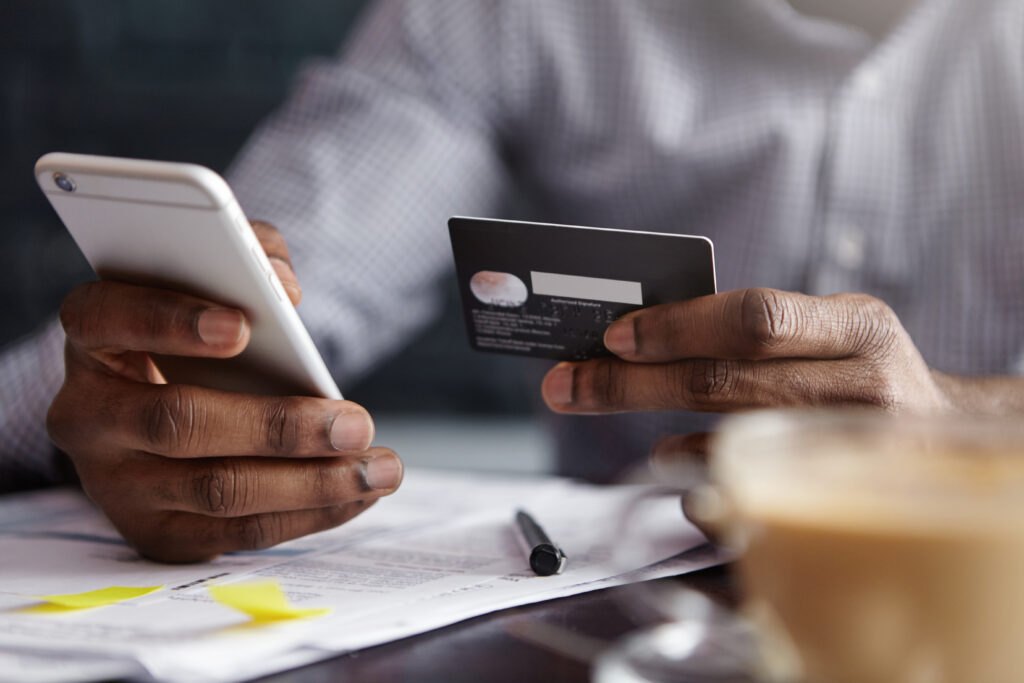 A businessman using a smartphone and a credit card to complete a transaction, demonstrating the ease of integrating BigCommerce Payment Gateways.
