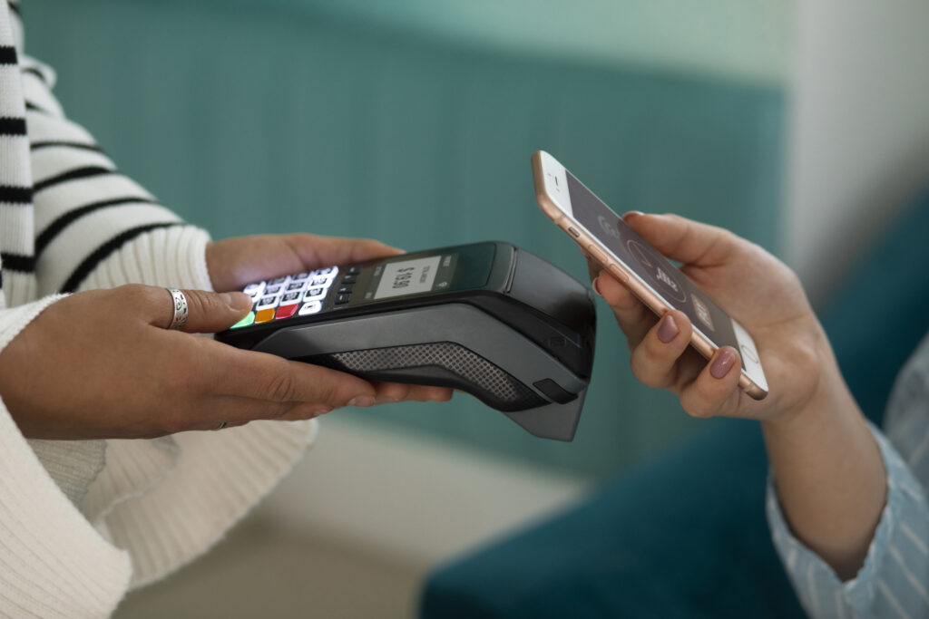 A person using a smartphone to make a contactless payment at a terminal, highlighting modern BigCommerce Payment Gateways in action.