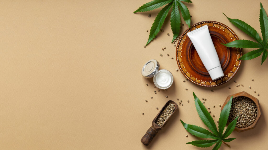 A top-down flat lay of CBD oil, cream jars, and green cannabis leaves on a neutral background, highlighting a shopify CBD skincare collection.